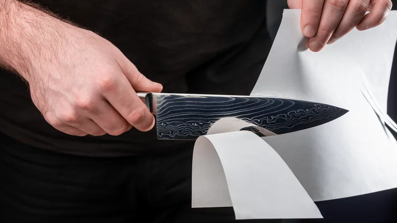 Chef knife slicing cleanly through a sheet of paper